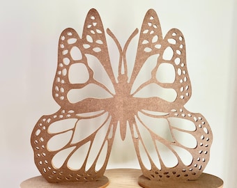 May include: A wooden butterfly cutout with intricate details, standing on two separate bases. The butterfly is a light brown color and has a delicate, lacy design.