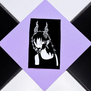 Può includere: Illustrazione in bianco e nero di un personaggio con corna e capelli lunghi. L'immagine è su un rettangolo nero, posto su un rombo viola, a sua volta su una superficie a scacchi in bianco e nero.