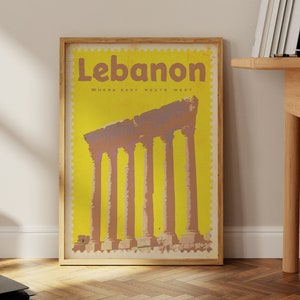 May include: A vintage travel poster with a yellow background and a brown frame. The poster features a photo of the Roman ruins of Baalbek in Lebanon. The text on the poster reads "Lebanon, Where East Meets West".