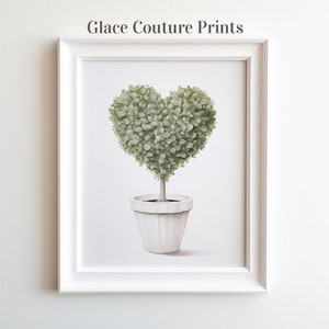 May include: A white framed print of a green heart-shaped topiary plant in a white pot. The print is titled "Glace Couture Prints".