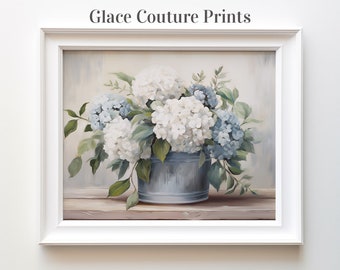 May include: A framed painting of a bouquet of white and blue hydrangeas in a blue metal bucket. The flowers are arranged in a rustic setting with a wooden surface and a light blue background.