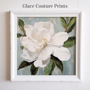 May include: A framed painting of a white magnolia flower with green leaves against a blue background. The painting is titled "Glace Couture Prints".