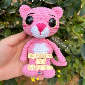 Puede incluir: Un juguete de pantera rosa hecho a mano con grandes ojos negros, detalles blancos y una nariz rosa. El texto "Digital item ONLY Pdf pattern" es visible. El juguete se sostiene frente a un fondo de hojas verdes.
