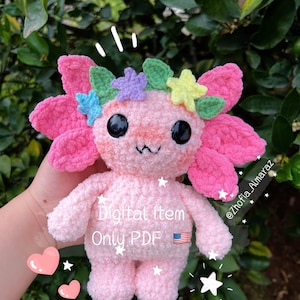 Puede incluir: Un peluche de ajolote rosa hecho a mano con grandes branquias en forma de pétalos y una corona de flores coloridas. El peluche tiene ojos negros de botón y una boca pequeña. El texto en el peluche dice "Digital item Only PDF" con una pequeña bandera estadounidense.