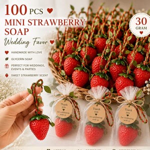 Op de afbeelding: Een set van 100 mini aardbei-vormige glycerine zepen, elk met een gewicht van 30 gram. De zepen zijn rood met groene blaadjes en bevestigd aan een rood-groen koord. Sommige zijn verpakt in doorzichtige witte organza zakjes met bruine labels.