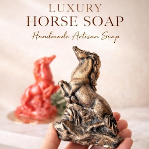 Op de afbeelding: Een bronzen paardzeepsculptuur wordt in een hand gehouden, met twee andere paardzepen op de achtergrond. De tekst luidt "LUXURY HORSE SOAP Handmade Artisan Soap". De zeep is gebeeldhouwd in de vorm van een steigerend paard.
