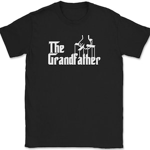May include: Black t-shirt with the white text "The Grandfather" and a graphic of a hand controlling puppet strings. The design is centered on the front of the shirt.