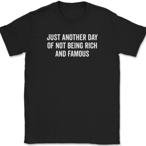 May include: Black t-shirt with white text that reads "Just another day of not being rich and famous."