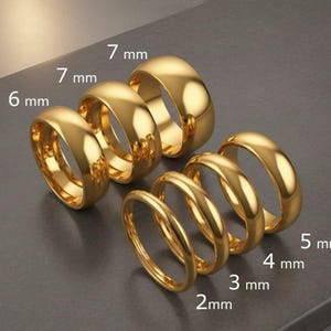 May include: A collection of gold-colored rings in various sizes, ranging from 2 mm to 7 mm in width. The rings have a polished, reflective surface, and are arranged to showcase the different widths available. The image highlights the different ring sizes.