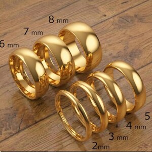 May include: A collection of gold-colored rings of varying widths, ranging from 2 mm to 8 mm. The rings are displayed on a wooden surface, with the ring sizes clearly labeled in millimeters.