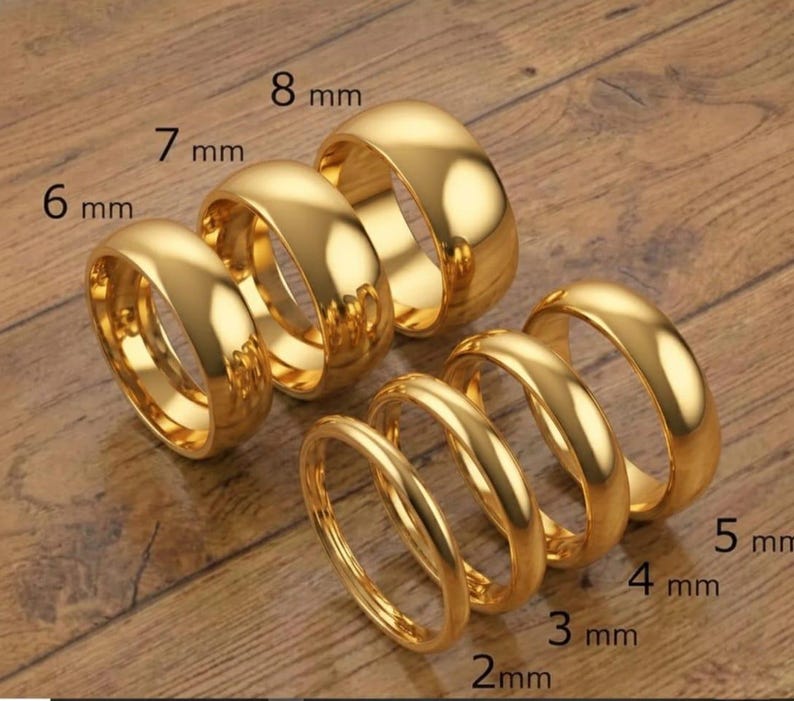 May include: A collection of gold-colored rings of varying widths, ranging from 2 mm to 8 mm. The rings are displayed on a wooden surface, with the ring sizes clearly labeled in millimeters.
