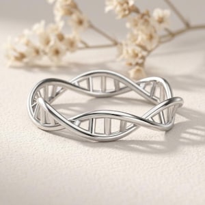 Könnte beinhalten: Ein silberfarbener Ring mit einer durchgehenden Doppelhelix-Struktur, die die Form eines DNA-Strangs nachahmt. Das Band besteht aus zwei ineinander verschlungenen Metallbändern, die durch kleine, gleichmäßig verteilte vertikale Stege verbunden sind.