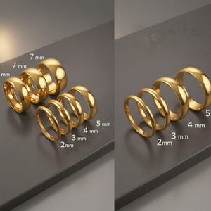 May include: A collection of gold-colored rings of varying widths, from 2 mm to 7 mm, displayed on a dark gray surface. The rings are arranged in two groups, showcasing different styles and sizes. The image highlights the different ring sizes.