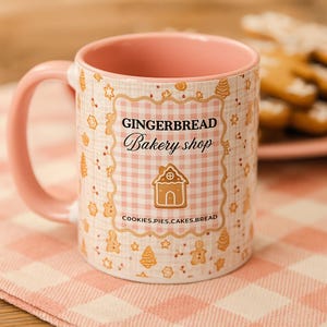 May include: A ceramic mug with a pink interior and handle, featuring a gingerbread theme. The mug is decorated with a pink and white checkered pattern and the words "GINGERBREAD Bakery shop". The design includes gingerbread house and cookie illustrations.