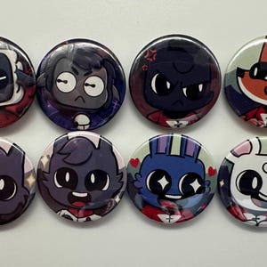 May include: Eight round button badges featuring cartoon characters with different expressions. The characters are a sheep, a fox, a rabbit, a cat, and three other characters with different coloured fur. The badges are all red, white and black.