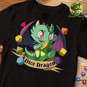 Puede incluir: Camiseta negra con un dragón verde de dibujos animados sosteniendo un dado. El dragón tiene alas moradas y está rodeado de dados coloridos. El texto "Dice Dragon" está escrito debajo del dragón.