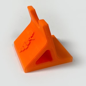 Può includere: Supporto per telefono arancione brillante con un design stilizzato a grappolo d'uva. Il supporto è realizzato in un materiale solido e ha una base triangolare con uno slot per un telefono. Il supporto è progettato per tenere un telefono in posizione verticale.