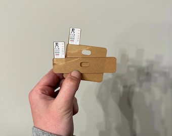 May include: Two eye charts are attached to a brown cardboard eye chart holder. The holder has two slots for the eye charts and a handle on the top.