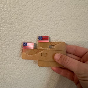 May include: A cardboard model of a building with two small American flags on top. The model is brown and has a textured surface.