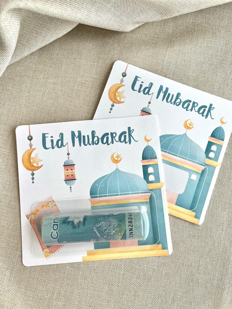 K&ouml;nnte beinhalten: Zwei wei&szlig;e Karten mit dem Text "Eid Mubarak" in blauer Schrift. Die Karten zeigen eine blaue Moschee mit einer goldenen Kuppel und einem Halbmond. Eine durchsichtige Plastiktasche auf der vorderen Karte enth&auml;lt einen kanadischen Dollar-Schein.
