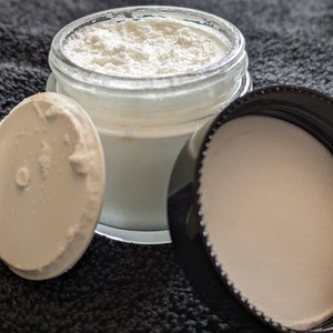 May include: A white powder in a clear glass jar with a white lid and a black lid. The jar is sitting on a black surface.