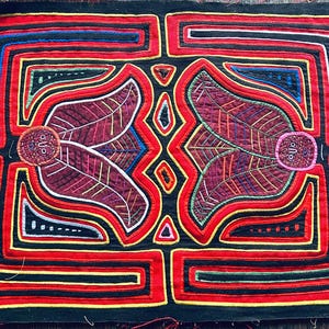 Puede incluir: Textil vibrante con un diseño simétrico. Presenta formas de hojas en borgoña, delineadas en rojo y negro. Los patrones geométricos con acentos amarillos, azules y blancos se colocan sobre un fondo negro. El textil es probablemente hecho a mano.