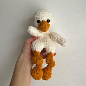 May include: White crocheted duck plush toy with orange legs.