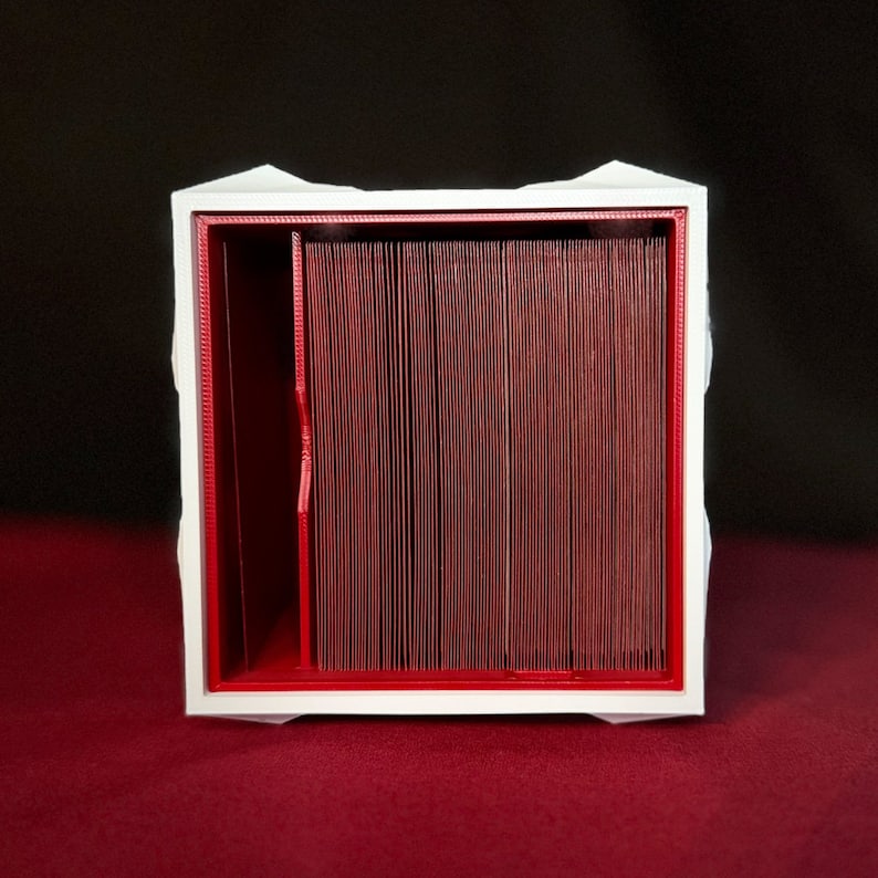 May include: White box with a red interior, designed to hold and organize cards. The box has a divider in the middle, creating two separate compartments.
