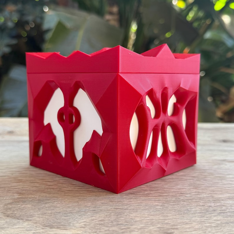 May include: A red geometric candle holder with a white interior. The holder has a unique, intricate design with cutouts.