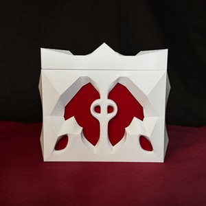 May include: White decorative box with a red interior and a geometric design. The box has a crown-like top and a cutout design on the front.