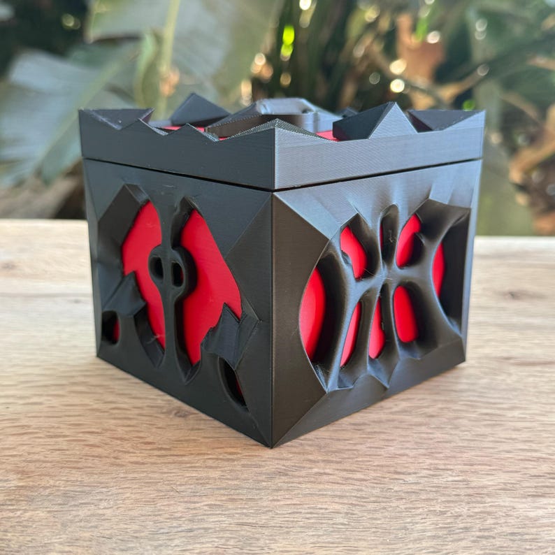 May include: A black 3D printed box with a red interior and intricate geometric designs. The box has a lid and is closed.