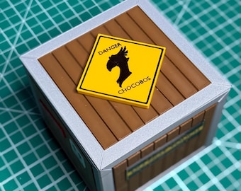 Könnte beinhalten: Eine braune Holzkiste mit silberner Umrandung und einem gelben Schild mit der Aufschrift "DANGER CHOCOBOS". Das Schild zeigt eine schwarze Silhouette eines Chocobo. Die Kiste hat eine rechteckige Form und ist aus Holz.