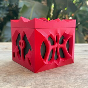 May include: A red, 3D printed box with a geometric design. The box has a textured surface and appears to be hollow.
