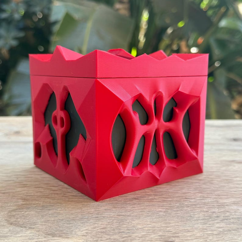 May include: A red, 3D printed box with a geometric design. The box has a textured surface and appears to be hollow.