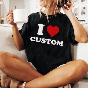 Op de afbeelding: Zwart T-shirt met witte tekst die "Ik hou van custom" zegt en een rood hart.