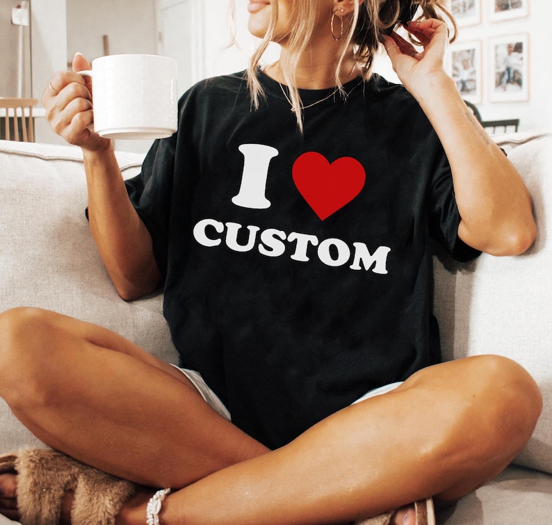Op de afbeelding: Zwart T-shirt met witte tekst die "Ik hou van custom" zegt en een rood hart.
