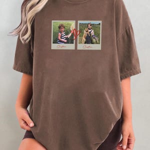May include: Brown t-shirt featuring two framed photos with children and a heart graphic. The photos are in a vintage style, with the word "Custom..." printed below each image. The shirt has short sleeves and a relaxed fit.