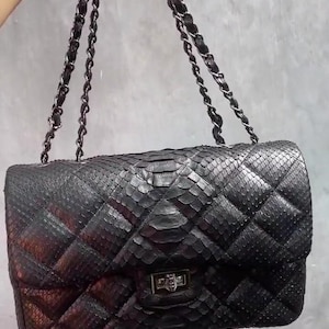 May include: A black quilted handbag with a silver chain strap and a silver clasp. The bag is made of snakeskin.