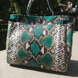 May include: A snakeskin-patterned handbag with a top handle and silver hardware. The bag features a mix of green, brown, and gray scales. The design includes a rectangular shape with a structured silhouette, suitable for carrying essentials.
