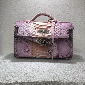 May include: A small, structured handbag with a top handle and a flap closure. The bag is made of pink and tan snakeskin with silver-tone hardware. The bag has a key charm and a small handle.