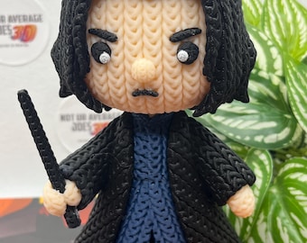May include: A 3D-printed figurine featuring a character with black hair, a beige face, and a serious expression. The figure wears a long black coat over a blue tunic and holds a black wand. The surface texture resembles a knitted pattern.