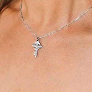 May include: A silver necklace with a key pendant featuring a Celtic cross design.