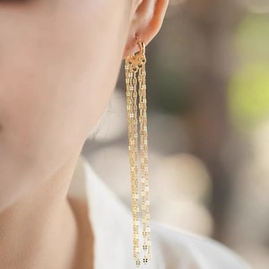 Puede incluir: Pendientes de aro dorados con múltiples cadenas que cuelgan de un pequeño aro. Las cadenas están hechas de pequeñas piezas ovaladas enlazadas.