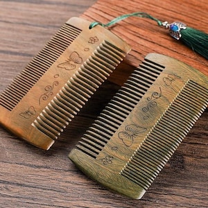 May include: Two wooden combs with intricate floral and butterfly designs. The combs are made of dark brown wood with green and gold accents.