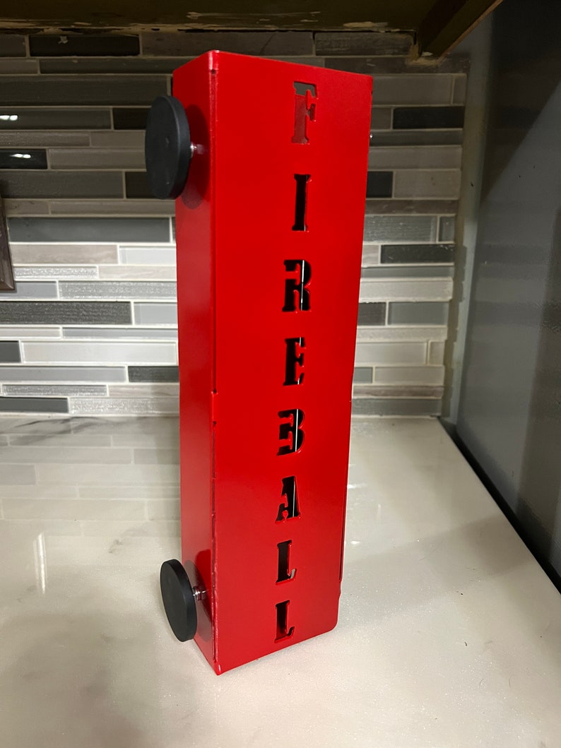 Op de afbeelding: Rode metalen brandkraan met het woord "FIREBALL" uitgesneden in zwarte letters. De brandkraan heeft zwarte wielen aan de onderkant.