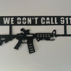 May include: Black metal wall art featuring a silhouette of a rifle with a scope and the text "WE DON'T CALL 911".