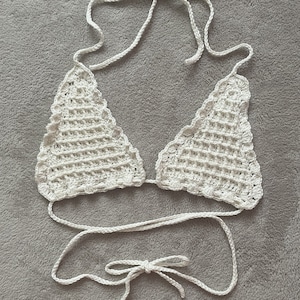 May include: White crochet bikini top with adjustable straps and a tie closure. The top is made of a delicate, open-weave fabric.