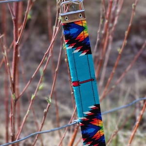 May include: A turquoise blue key chain with a colorful geometric pattern. The key chain is attached to a silver key ring.