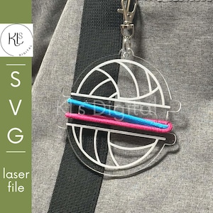 Peut inclure: Un porte-clés circulaire en acrylique transparent avec un motif de ballon de volley-ball gravé en blanc. Le design présente une découpe horizontale où un cordon élastique bleu vif et un rose sont insérés, fixé à un mousqueton en métal argenté.