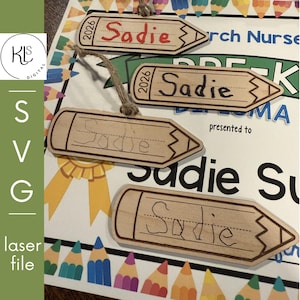 May include: Wooden pencil-shaped ornaments with the name "Sadie" written on them. Some ornaments have the year "2026" on them. The ornaments are on a background with a diploma and colorful pencil illustrations.